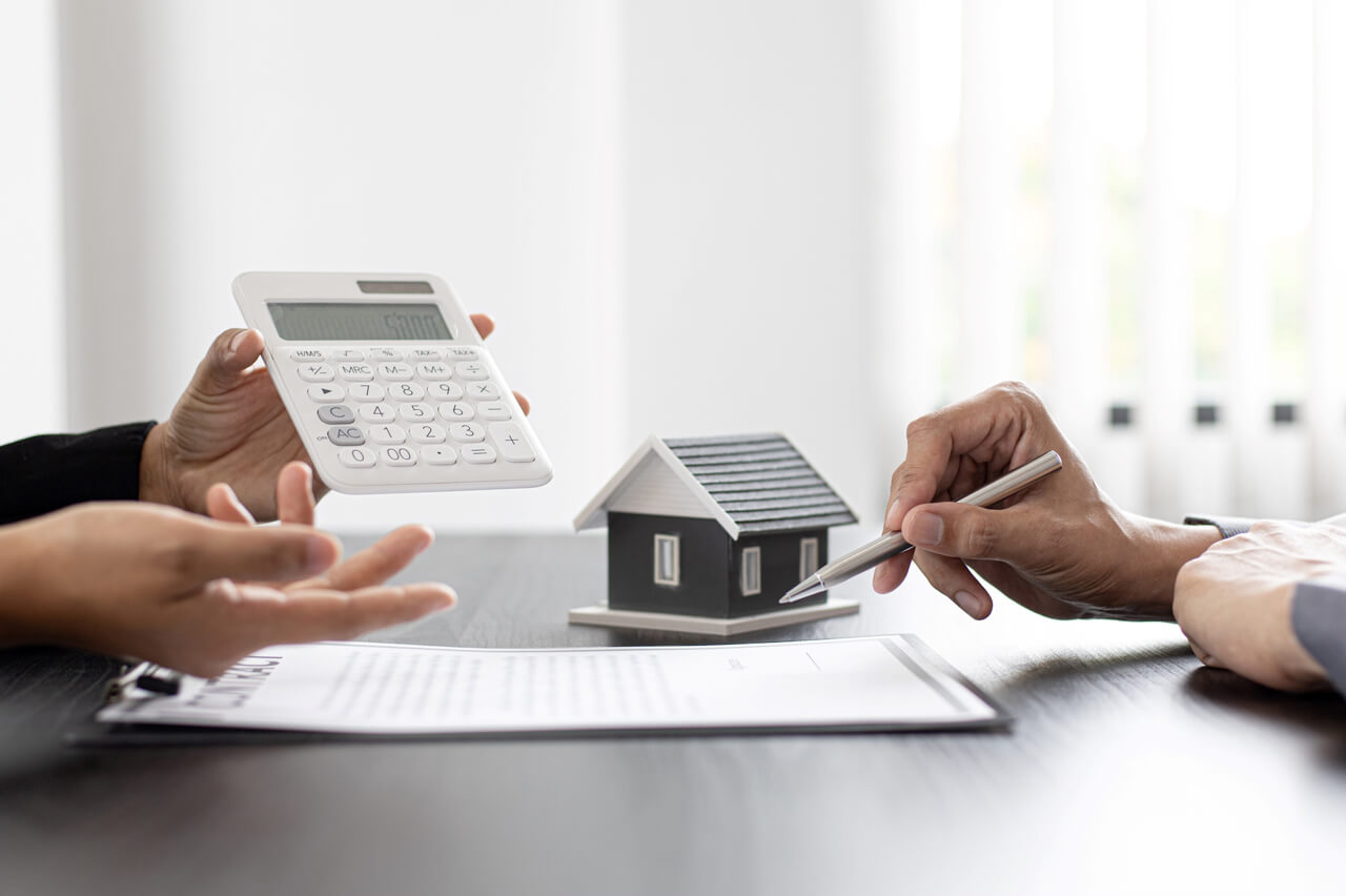 Grundsteuererklärung- Bild mit kleinem Haus, Taschenrechner und Stift in der Hand und Notizblatt